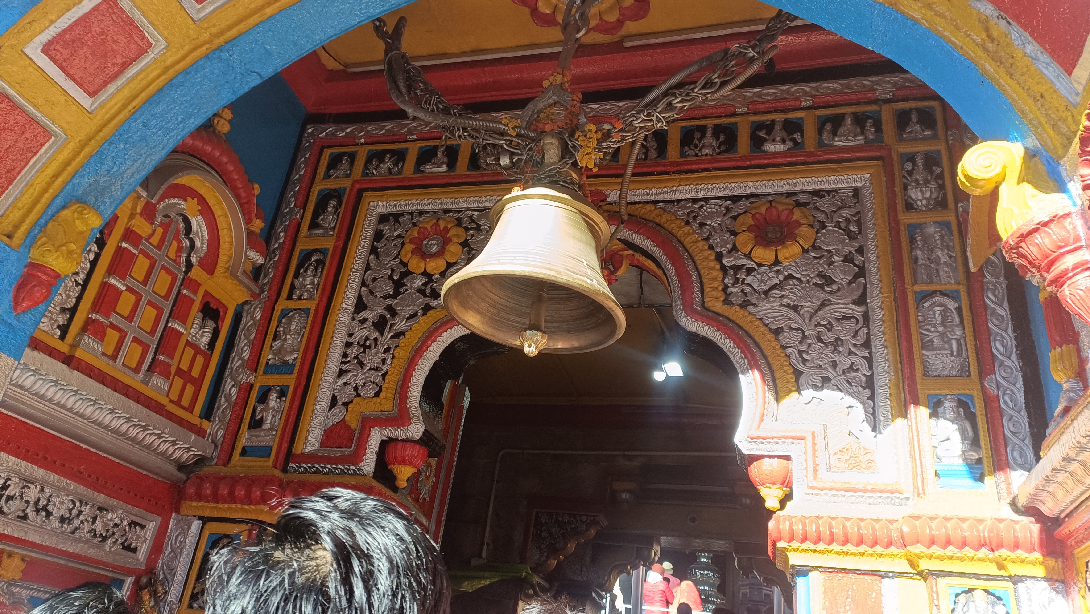बद्रीनाथ मंदिर के प्रवेश द्वार पर लटका घंटा और रंगीन सजावट