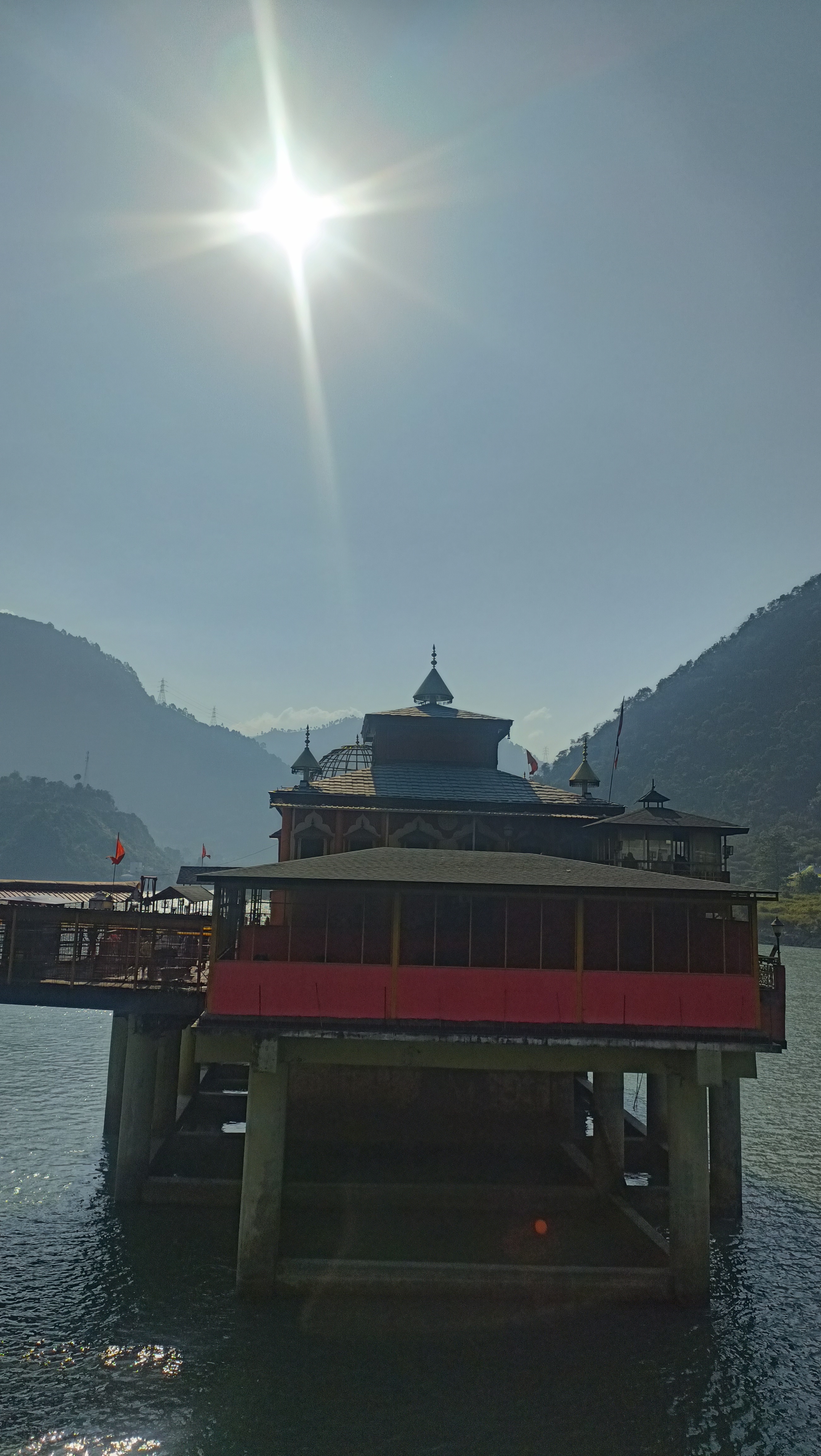 नदी के ऊपर धारा देवी मंदिर, पीछे पहाड़ और धूप