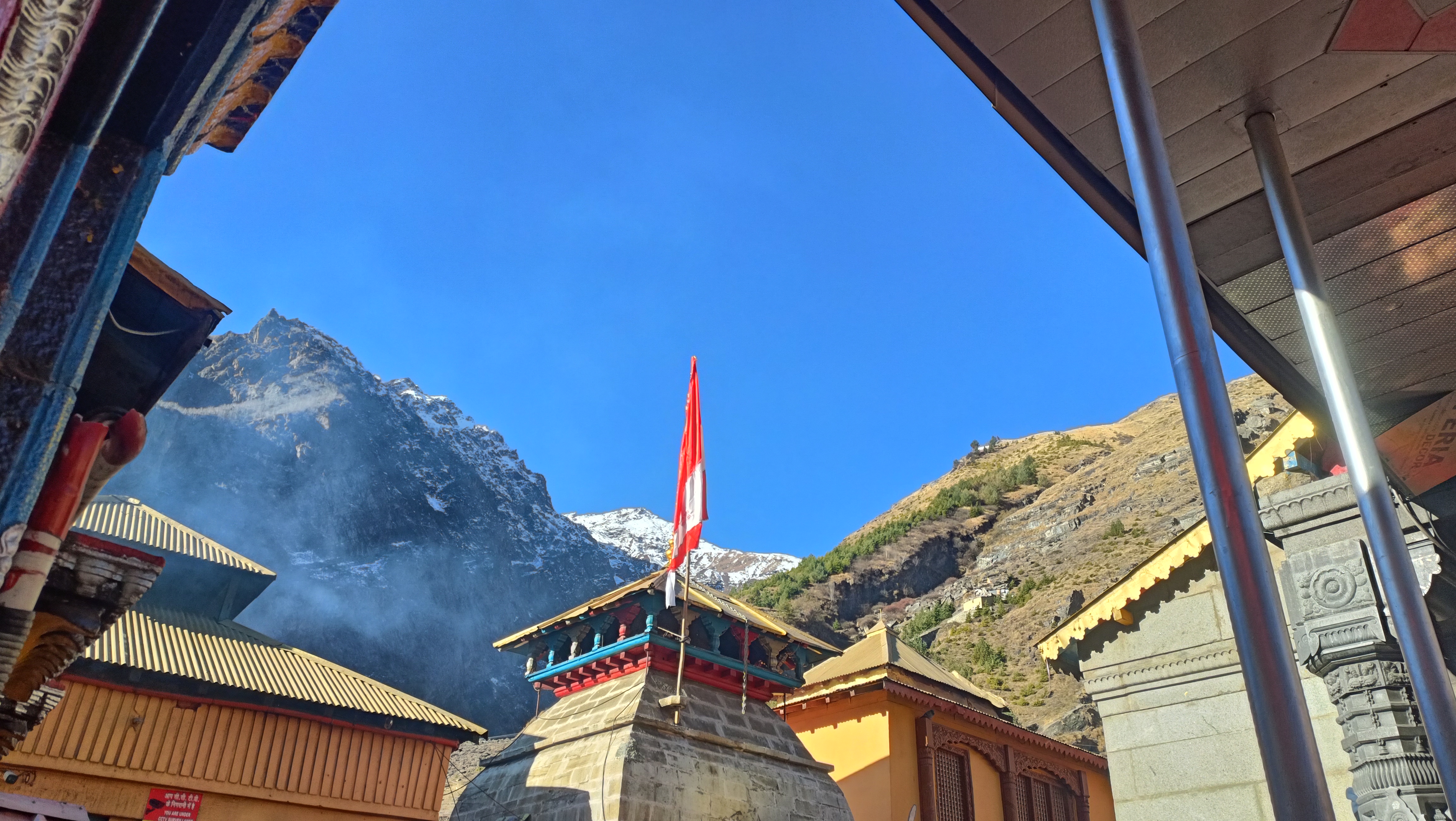 बद्रीनाथ मंदिर प्रांगण से पहाड़ और ध्वज का दृश्य